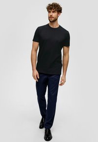 Camiseta negra de cuello redondo combinada con pantalones azul marino y zapatos negros. La camiseta es ajustada y el tejido parece suave, sin patrones.
