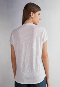 T-shirt bianco a maniche corte con vestibilità rilassata e scollatura rotonda. Tessuto morbido e leggero con una leggera trasparenza, con orlo curvo.