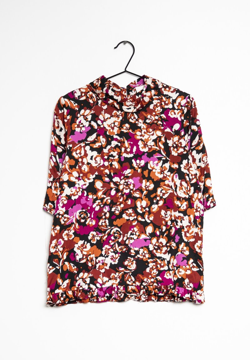 Blouse fleurie avec un fond noir, ornée de fleurs vibrantes orange, rose et blanches. Tissu doux avec un ourlet volanté et un col montant simulé.