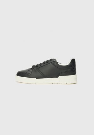 Baskets en cuir noir avec une semelle blanche, dotées de six œillets et de détails en couture, présentées en vue latérale sur fond uni.