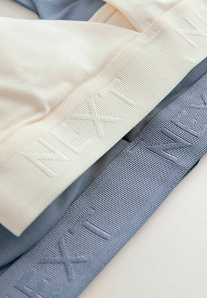 Dwa wyroby tekstylne ułożone w stos: kremowy i jasnoniebieski elastyczny materiał. Każdy z nich ma teksturowany pas z wytłoczonym w powtarzającym się wzorze napisem "NEXT".