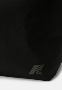 Black fabric bag featuring a matte logo with geometric line design. The texture appears smooth, with a structured, angular shape.