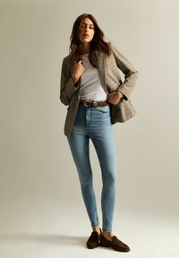 Rutig brun blazer över en vit t-shirt, i kombination med ljusblå skinny jeans och bruna slip-on skor. Slät tygkvalitet och skräddarsydd passform.