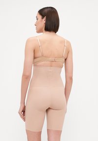 Bežna oblikovalna bodysuit z nastavljivimi naramnicami, visoko pasom in gladkim, raztegljivim materialom. Ima perforirane detajle na hrbtu.