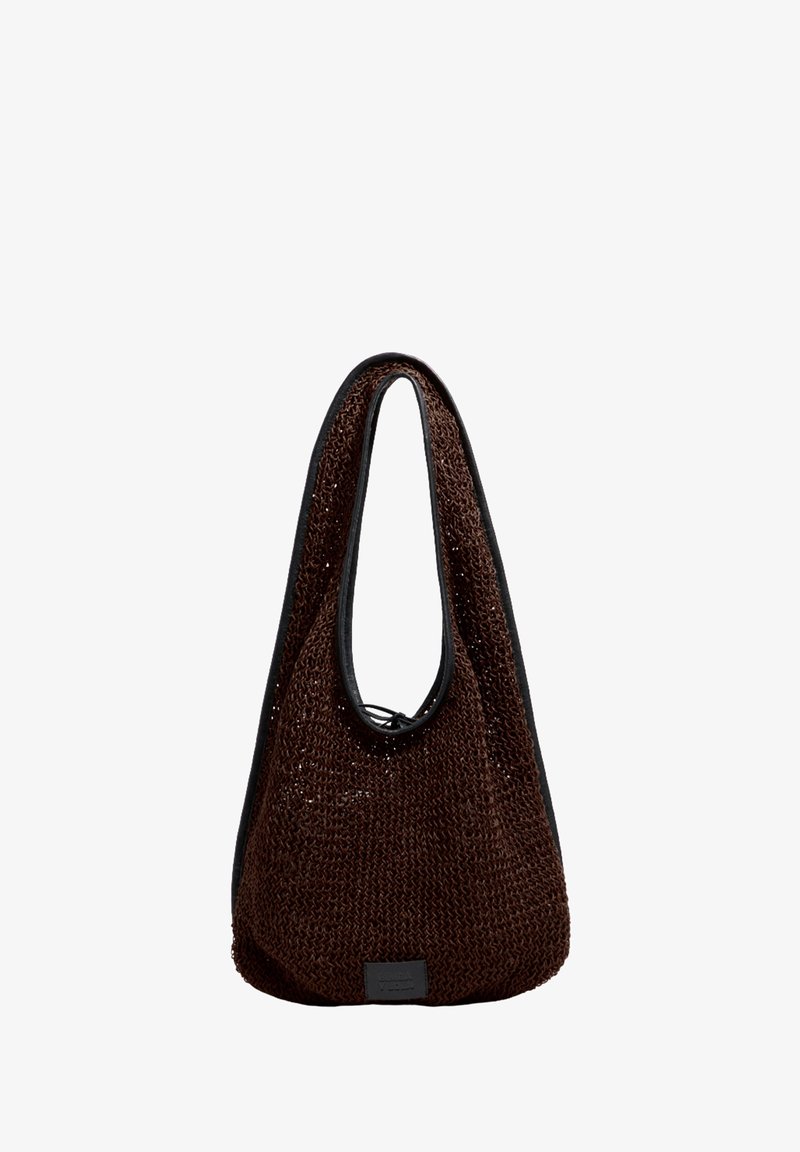 Bolso marrón tejido con textura suave, con asa de lazo y borde negro a contraste. Incluye una pequeña etiqueta en el lateral.