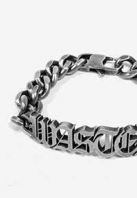 Bracciale in metallo argento con catene spesse e un'incisione stilizzata della parola "Wasted". Presenta una chiusura a moschettone.