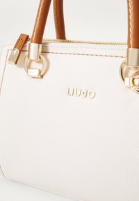Borsa in pelle rosa chiaro con manici marroni, dettagli in hardware dorato e il marchio impresso "LIU•JO" sul fronte. Chiusura con cerniera.