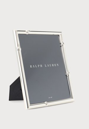 Strieborný obdĺžnikový rám na fotografiu s bambusovým vzhľadom hrán stojaci na čiernej podpere a zobrazujúci text "Ralph Lauren".