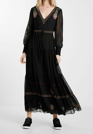 Black long dress with floral embroidery, sheer puff sleeves, smocked cuffs, a V-neckline, and sneakers on a standing person.