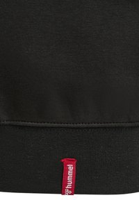 Schwarzer Stoff mit einer genähten Naht über einem roten Stoffetikett mit der Aufschrift „hummel“ in weißer Schrift unten in der Mitte.