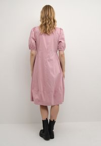 Rosa knälång klänning med korta puffärmar, åtsittande midja och en slät yta. I kombination med svarta ankle boots.
