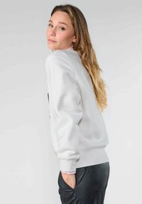 Sudadera de cuello redondo en tejido gris claro, con un corte relajado, puños y dobladillo acanalados. Combinada con pantalones jogger negros con textura.