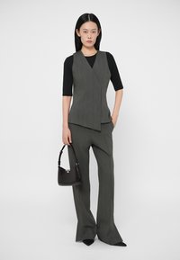 Gilet grigio doppiopetto con finitura testurizzata, abbinato a pantaloni grigi a gamba larga. Una borsa nera con motivo lucido effetto coccodrillo completa il look.