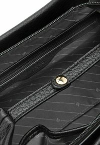 Wnętrze czarnej skórzanej torebki z kieszenią na suwak i paskiem na zatrzask, o gładkiej fakturze i wzorze z ukośnymi liniami na tkaninie.