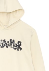 Felpa crema con cappuccio regolabile. Presenta scritte in stile graffiti nero sulla parte anteriore. Realizzata in stoffa testurizzata con una vestibilità comoda.