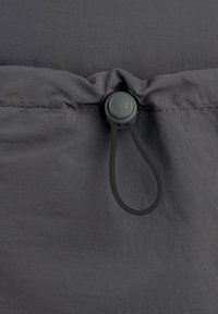 Un tissu gris au toucher lisse présente une couture froncée et un toggle en plastique avec une boucle élastique pour l'ajustement.