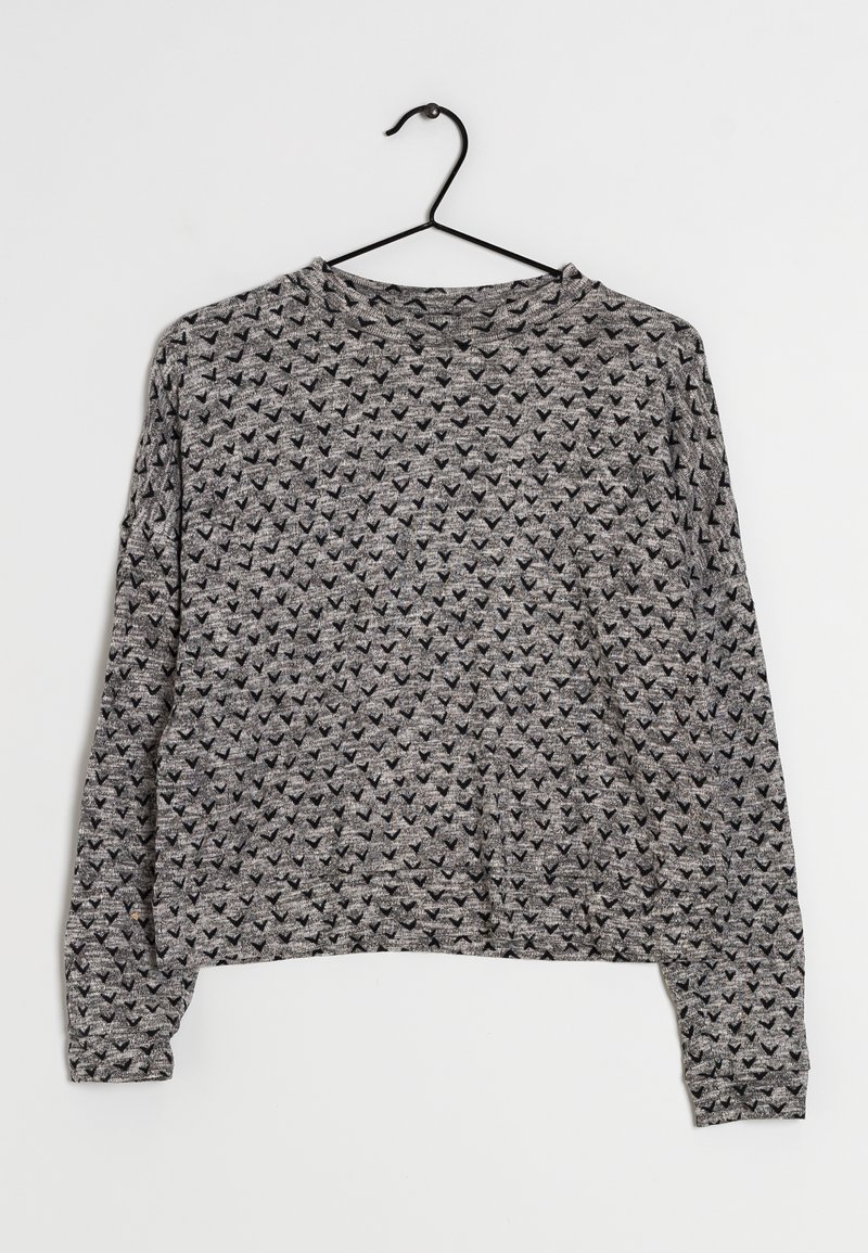 Gray long-sleeve sweater with a textured pattern of small black triangles, round neck, cropped fit, and a smooth knit fabric. Hangs on a black hook.