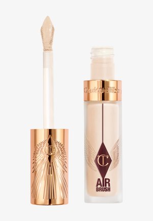 Liquid concealer in a frosted glass bottle with a gold top, featuring embossed wings and a pointed applicator. Color: light beige.