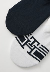 Two pairs of ankle socks: one navy blue, one white with a navy geometric pattern and black accents, made from a soft, stretchy material.