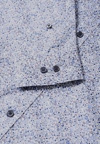 Blommönstrad skjorta i ljusblått och vitt, med små blommor i blått och rosa. Detaljer inkluderar svarta knappar och en slät textur.