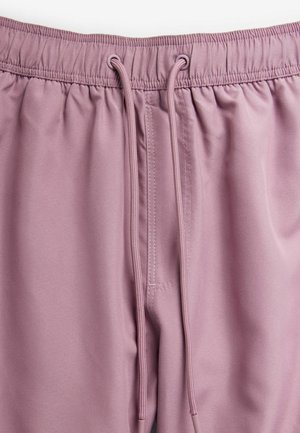 Svetlo roza elastični joggerji z naramnicami, gladka tekstura in stranski žep. Imajo šivane podrobnosti ob pasu.