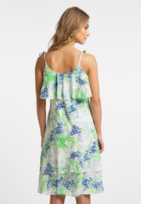 Blumenkleid mit geschichteten Rüschen auf der Rückseite, in Blau- und Grüntönen auf hellem Hintergrund. Verstellbare Spaghettiträger.