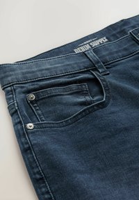 Tmavomodré džínsy z denimu s klasickým návrhom piatich vreciek, s etiketou na páske a striebornými kovovými doplnkami.