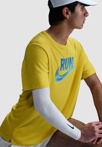 Camiseta amarilla de manga corta con un gráfico azul de "RUN" y el swoosh de Nike, combinada con una manga blanca, mostrando un diseño deportivo.