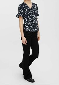 Blusa avvolgente nera a fiori con maniche corte a volant, dotata di scollatura a V e dettaglio di legatura laterale. Abbinata a pantaloni neri a zampa.
