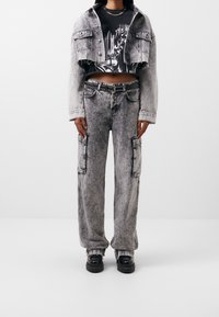 Harmaa happopesu farkkutakki ja cargo-housut, yhdistettynä mustaan graafiseen t-paitaan. Varusteena niittivyö mustana ja tukevat mustat kengät.