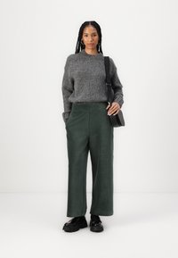 Maglione grigio lavorato a maglia, pantaloni a gamba larga in velluto a coste verde, scarpe con plateau nere e una piccola borsa a tracolla nera; texture liscia e vestibilità rilassata.