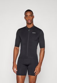 Combinaison de cyclisme noire à manches courtes et fermeture éclair à l'avant. Fabriquée en tissu lisse et extensible. Présente un logo discret sur la poitrine gauche.