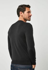 Pulover negru tricotat, cu guler rotund, mâneci lungi și tiv ribstit. Textură netedă, design ajustat și detalii minime.