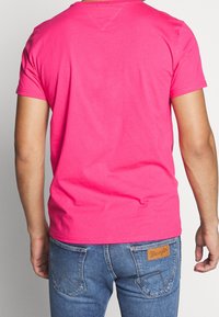 Camiseta ajustada de algodón rosa con mangas cortas, cuello redondo y textura suave, combinada con jeans de mezclilla azul que presentan una etiqueta de cuero.