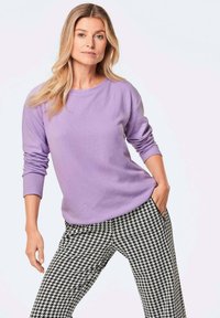 Lavendel Crewneck-Pullover mit langen Ärmeln, kombiniert mit einer lässigen Passform von Hosen im schwarz-weißen Hahnentrittmuster, weiche Textur.
