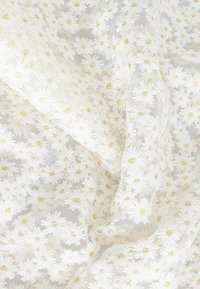 Tissu blanc avec broderies florales, présentant de petites marguerites et des accents dorés, possède une texture légère créant une apparence délicate.