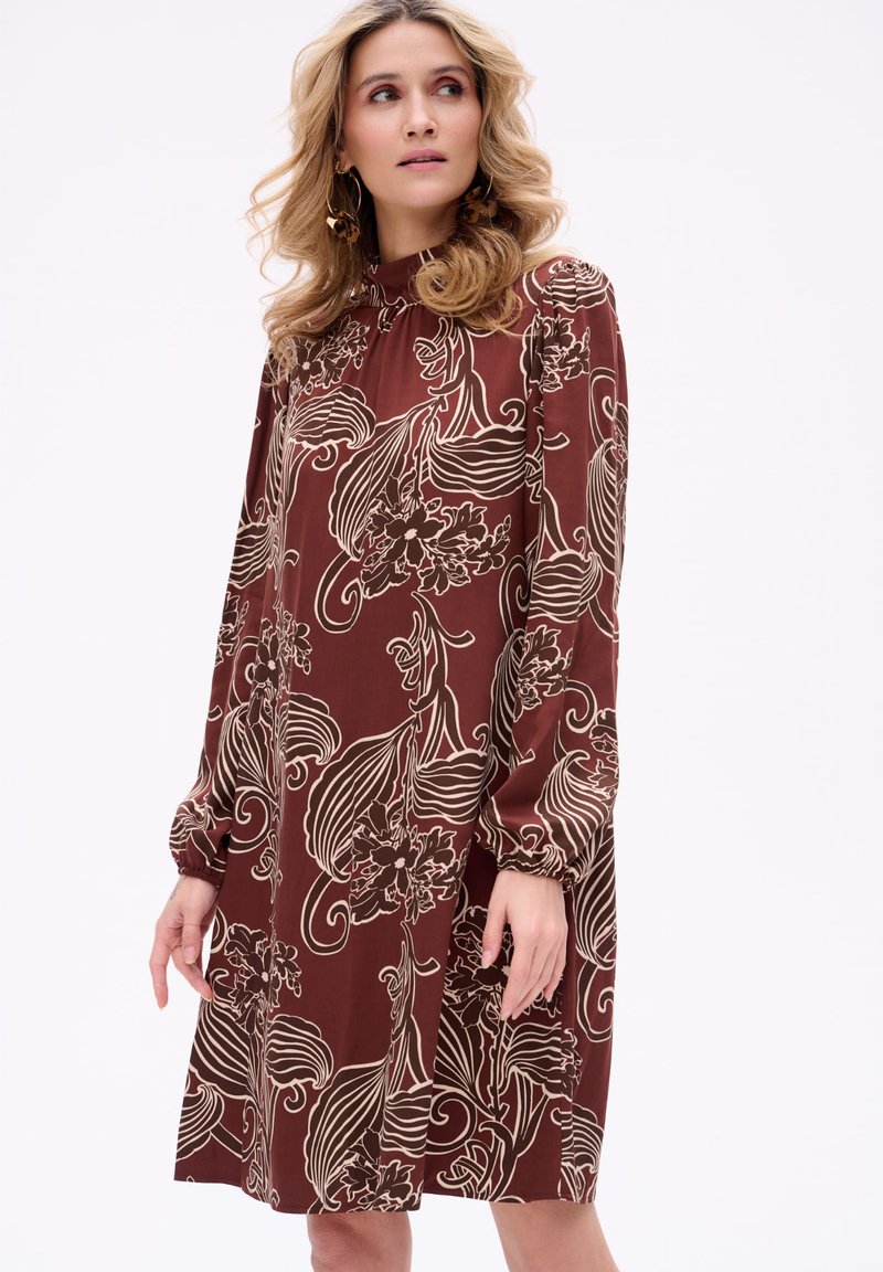 Czekoladowa długa sukienka w kwiaty z długimi rękawami, wysokim kołnierzem, bufkami oraz misternymi białymi wzorami kwiatowymi na jedwabnym materiale.