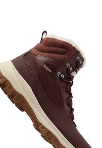 Scarponi da trekking impermeabili marroni con tomaia testurizzata, collo imbottito, bordo in pile bianco e suola in gomma robusta. Presenta occhielli in metallo e lacci.