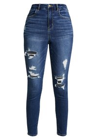 Mörkblå högmidjade skinny jeans med slitna hål på båda låren, som visar randiga tyglappar under.