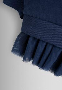 Tengerészeti pamut ruházat szegélye fodros hálóborítással. A háló lágy textúrájú, és áttetsző, pöttyös mintázatú a szélén.