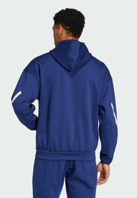 Sudadera azul marino con cordón y puños de canalé, que presenta una banda de acento blanca en las mangas, confeccionada en una tela suave y texturizada.