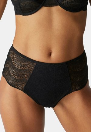 Frau trägt schwarze hoch taillierte Spitzenunterwäsche mit gewellten Mustern und passenden schwarzen Spitzen-BH, gezeigt vom Bauch bis zu den oberen Oberschenkeln.