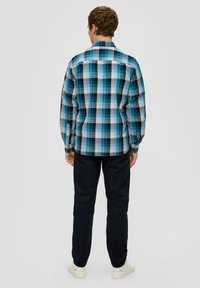 Blauw-wit geruite overhemd met lange mouwen en knoopmanchetten, gecombineerd met donkere broek en witte sneakers, gezien vanuit de achterkant.