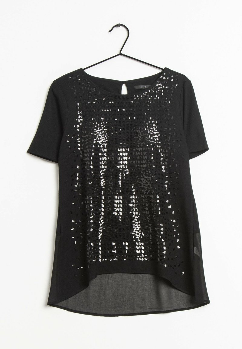 Blouse noire à manches courtes avec col rond, sequins sur le devant, bouton en forme de clé à l'arrière et un ourlet légèrement transparent asymétrique, accrochée à un cintre noir.