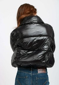 Giacca a vento nera con finitura lucida, colletto corto e texture trapuntata. Abbinata a jeans blu a vita alta con tasche posteriori.