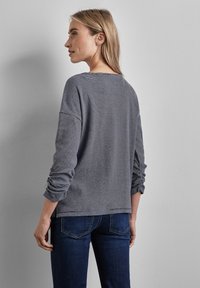 Gestreiftes Langarmshirt mit lockerer Passform, ausgestattet mit hochrollbaren Ärmeln, grauen und weißen horizontalen Streifen sowie einem abgerundeten Ausschnitt.