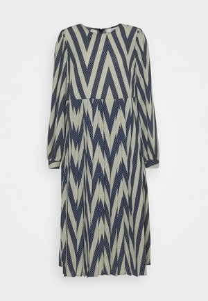 Robe à manches longues avec une base crème, un motif en zigzag bleu marine et des pois, un col rond et une silhouette fluide.