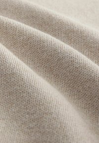 Beige rakennekangas hienolla neulekuviolla, joka esittelee hienovaraisia värivaihteluita ja pehmeän, hieman koholla olevan pinnan.