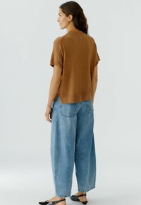 Brown short-sleeve sweater met een relaxed fit, gecombineerd met lichtblauwe baggy jeans. Opvallende knoopdetails op de rug en een gladde textuur.