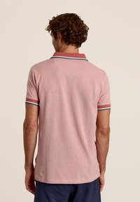 Polo shirt rose à manches courtes, avec un col contrastant et des bordures de manches en bleu et rouge. Tissu doux, coupe décontractée et fentes latérales à l'ourlet.